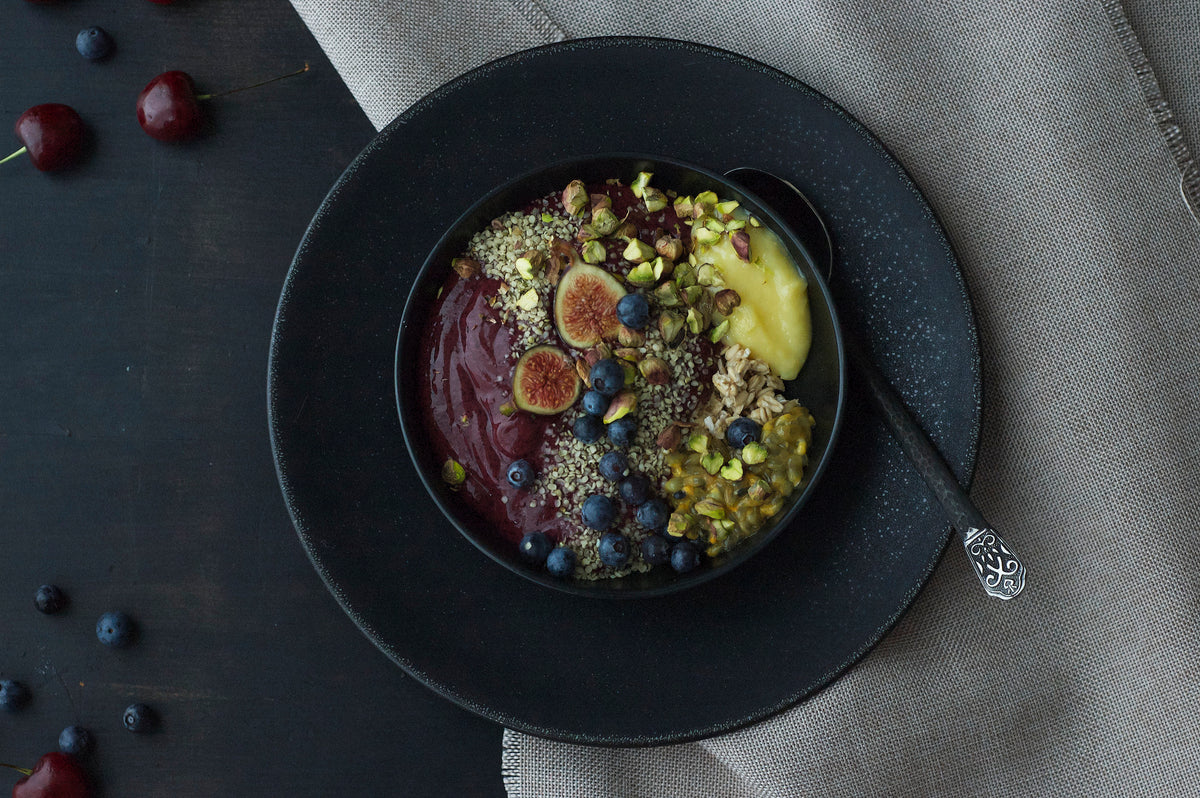 Acai smoothie bowl with figs and pistachios in black ceramic bowl, holistic wellness nutrition by Elena Dragoi